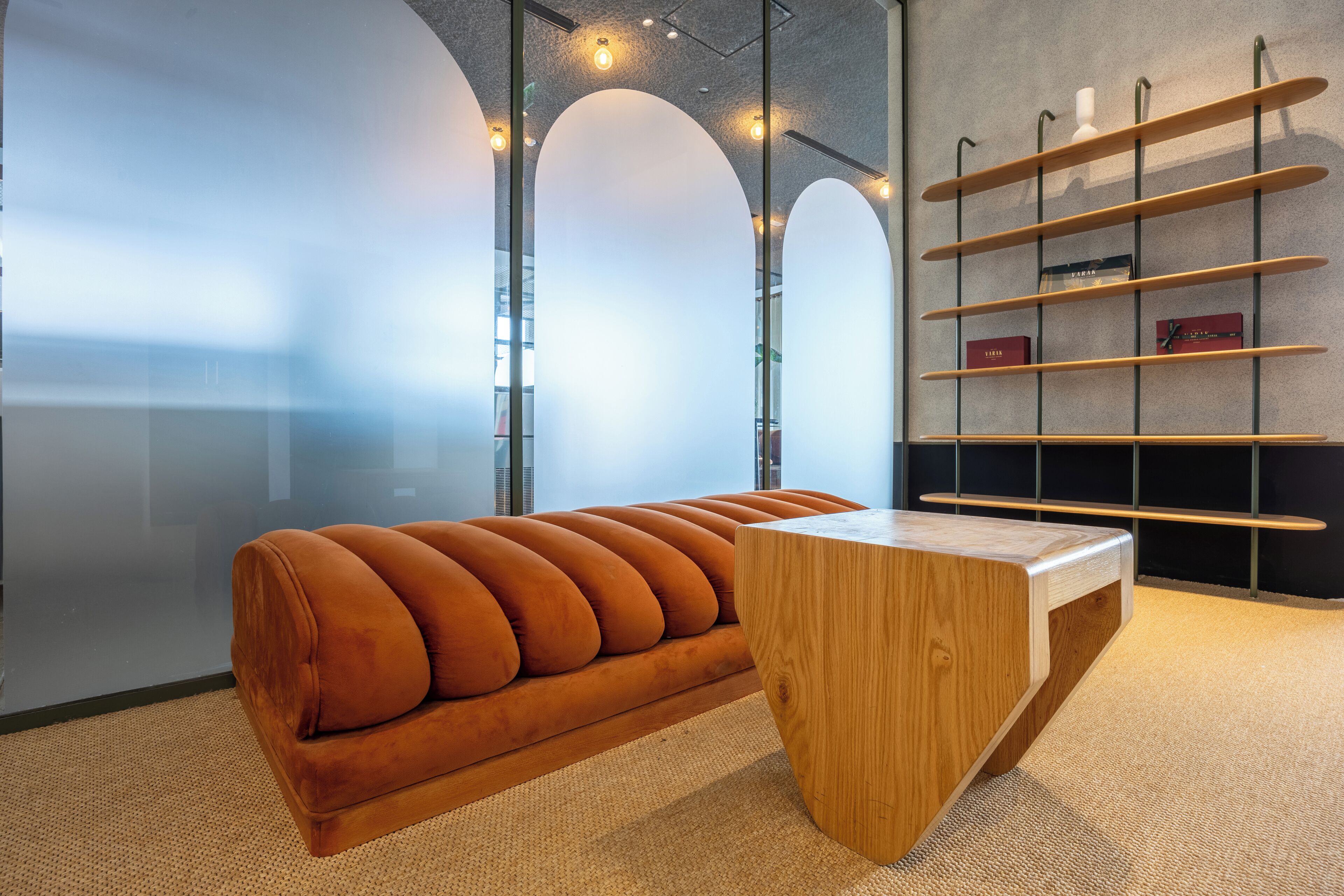 A modern office space with a wooden bench, a glass wall, and a shelving unit with books and decorative items.