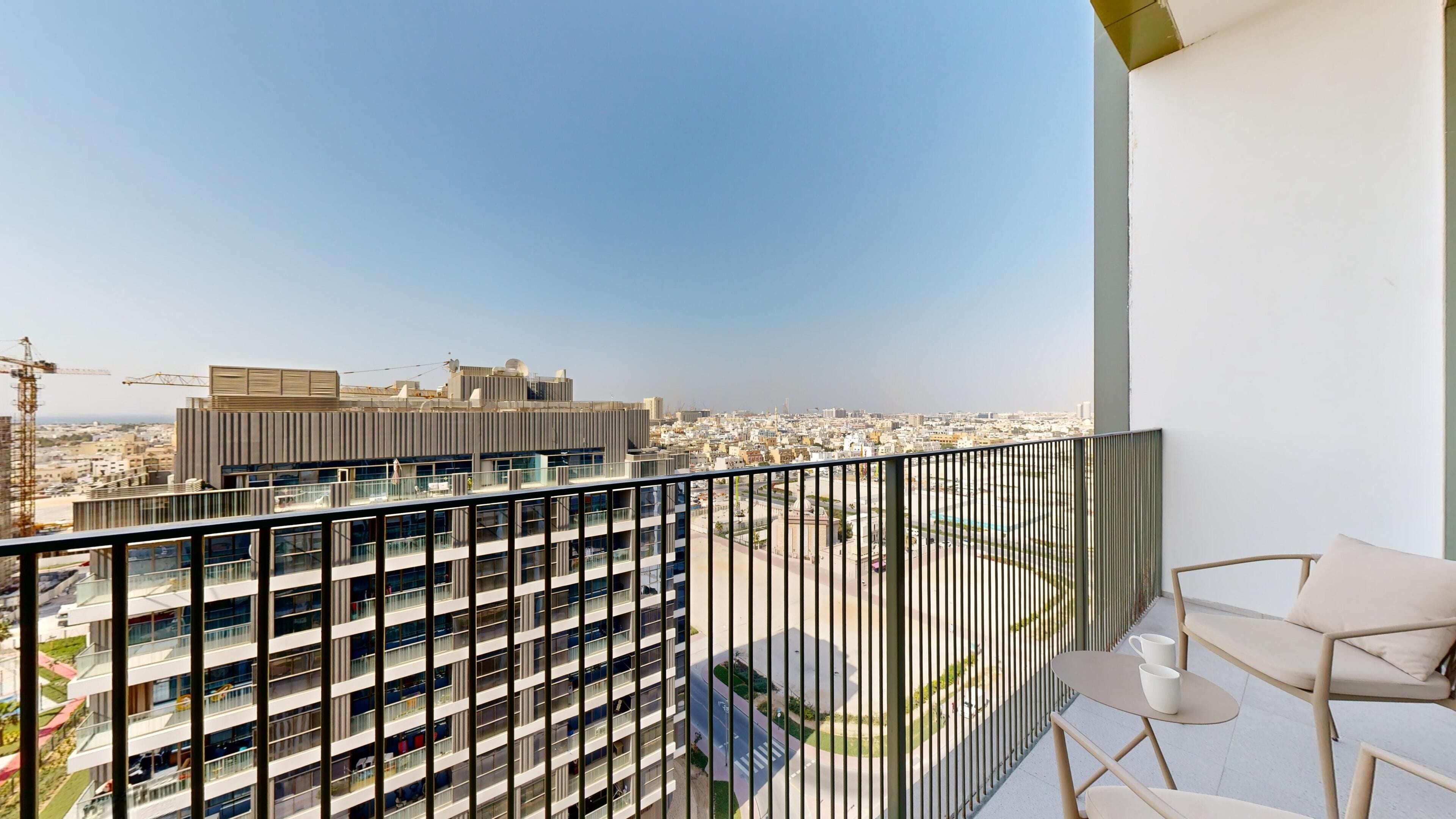 Um edifício alto com várias varandas, vista para a paisagem urbana e uma varanda com mesa e cadeiras.