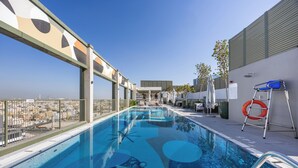 Una piscina en la azotea con agua cristalina y azul, rodeada por una barandilla metálica y con vistas a un paisaje urbano.