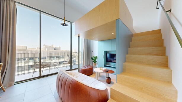Una sala de estar moderna con un gran ventanal, un sofá de cuero marrón, una mesita redonda y una escalera.
