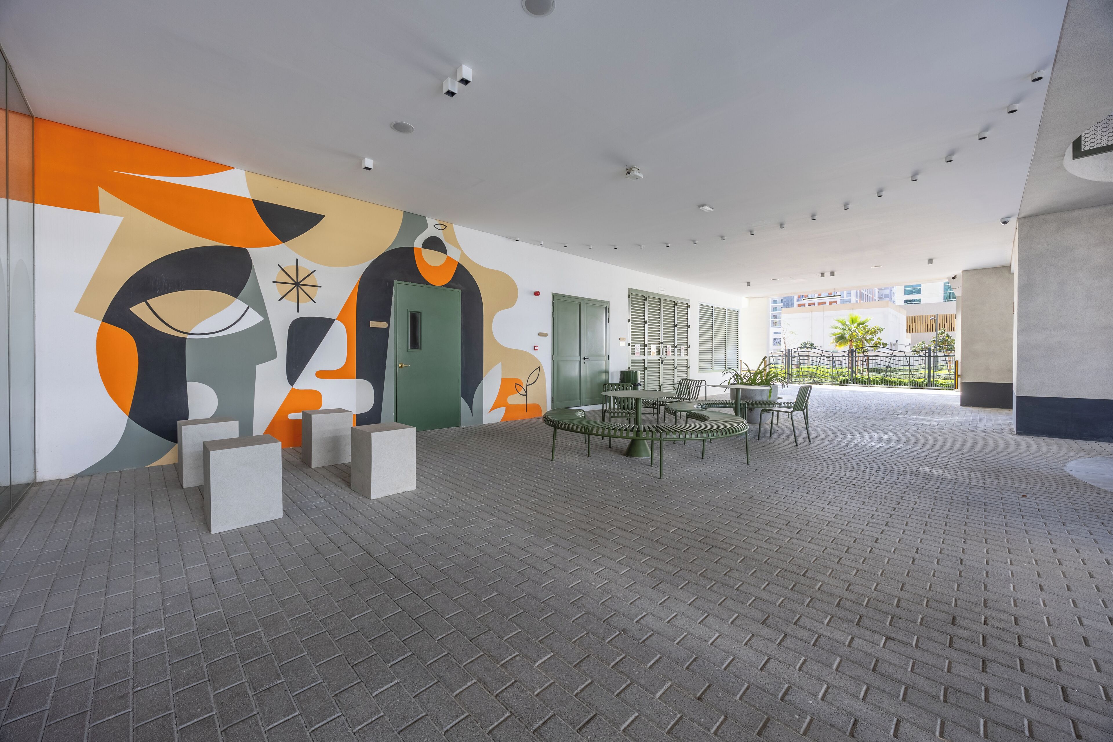 Ein moderner Innenraum mit Wandgemälde im geometrischen Stil, einer grünen Tür und einer Sitzgruppe mit Tischen und Stühlen.