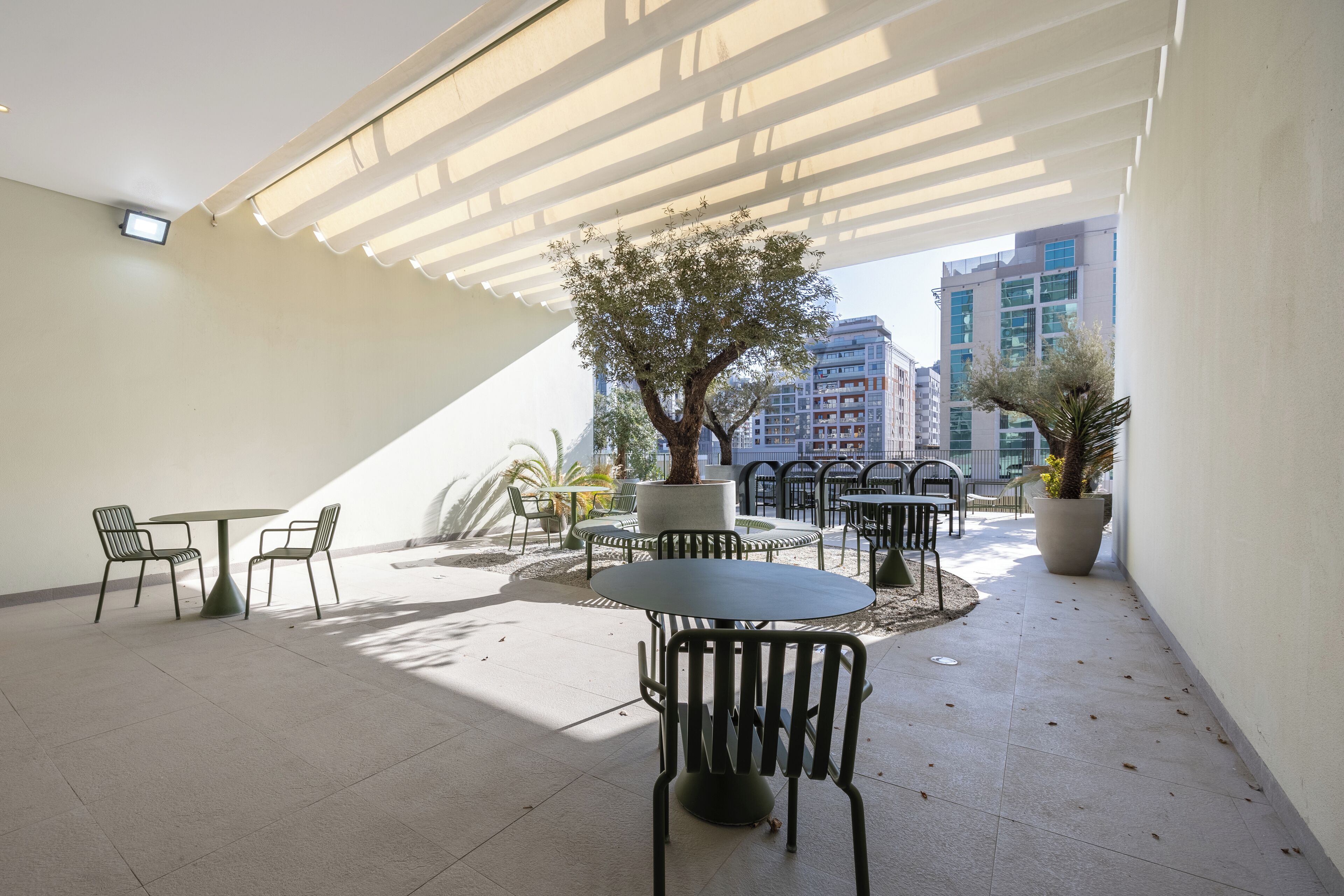 Un'area patio esterna con tavoli e sedie, un grande albero e piante in vaso.