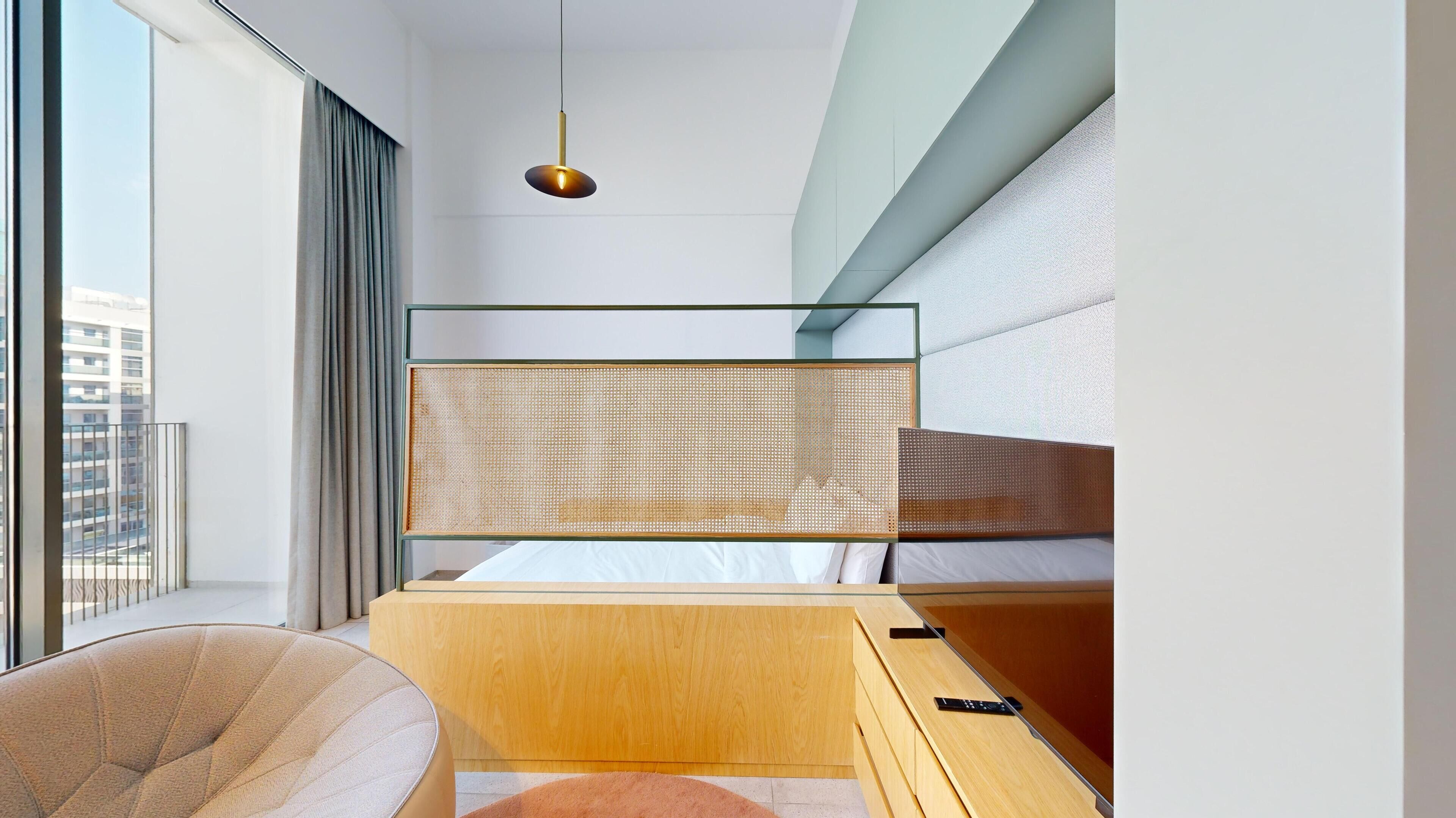 Un dormitorio moderno con separador de vidrio, un escritorio de madera, una silla y una lámpara colgante.
