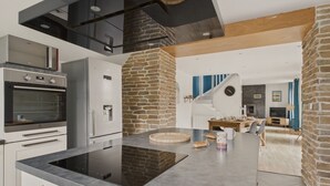 Cocina moderna con estufa, horno y refrigerador integrados. Presenta un muro decorativo de piedra y techo con vigas de madera.