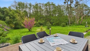 Un área de comedor al aire libre con una mesa preparada para cuatro personas, rodeada de abundante follaje y árboles.