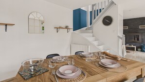 Un comedor con una mesa de madera dispuesta para cuatro, una escalera con detalles azules y una cocina moderna al fondo.