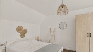 Un dormitorio con cama, armario, mesita de noche, lámpara, escalera y adornos en la pared.