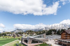 A modern building with a unique angular design, surrounded by a lush green field and a mountainous backdrop. - Apartment overlooking the slopes, for 8 people (Le Dévoluy)