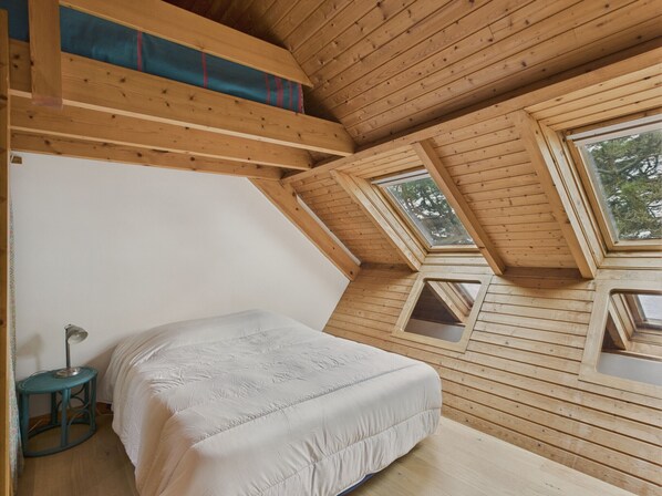 A bedroom with a sloped ceiling, wooden beams, and skylights.