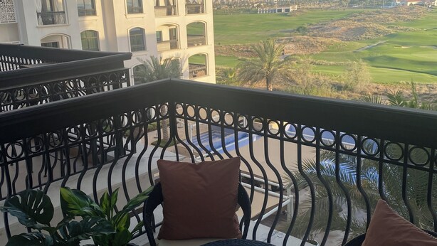 Un balcón con vistas a un campo de golf, un edificio con ventanas de arco y una piscina.