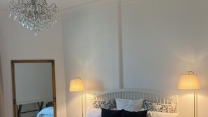 Una cama bien hecha con sábanas blancas, dos lámparas de noche, un espejo grande y un candelabro.