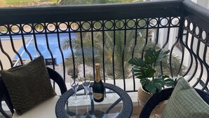 Un balcón con dos sillas, una mesa y una botella de champán. El balcón ofrece vistas a un campo de golf y una masa de agua.