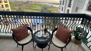 Un balcón con dos sillas y una mesita, con vistas a un campo de golf y una masa de agua.