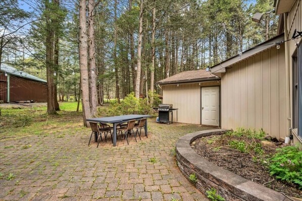 A backyard with a paved patio, a table with chairs, a barbecue grill, and a shed. - Tranquil Pocono Escape (Blakeslee)