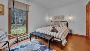 A bedroom with a bed, a window with a view of trees, a chair, a bench, and a ceiling fan. - Tranquil  Pocono Escape (Blakeslee)