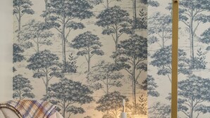 Una habitación con papel tapiz estampado, un sillón mecededor de madera, una mesita de noche y una lámpara.