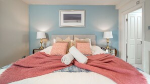 A bedroom with a bed, two bedside tables, a framed picture on the wall, and a door to the right.