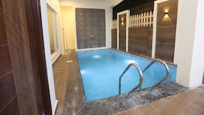 A swimming pool with a blue tiled floor, a metal ladder, and a white picket fence. - MM Beach House (Tirupporur)