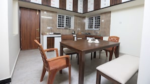 A modern kitchen with wooden cabinets, a dining table, and chairs. - MM Beach House (Tirupporur)