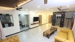 A modern living room with a sofa, coffee table, and a TV mounted on the wall. - MM Beach House (Tirupporur)