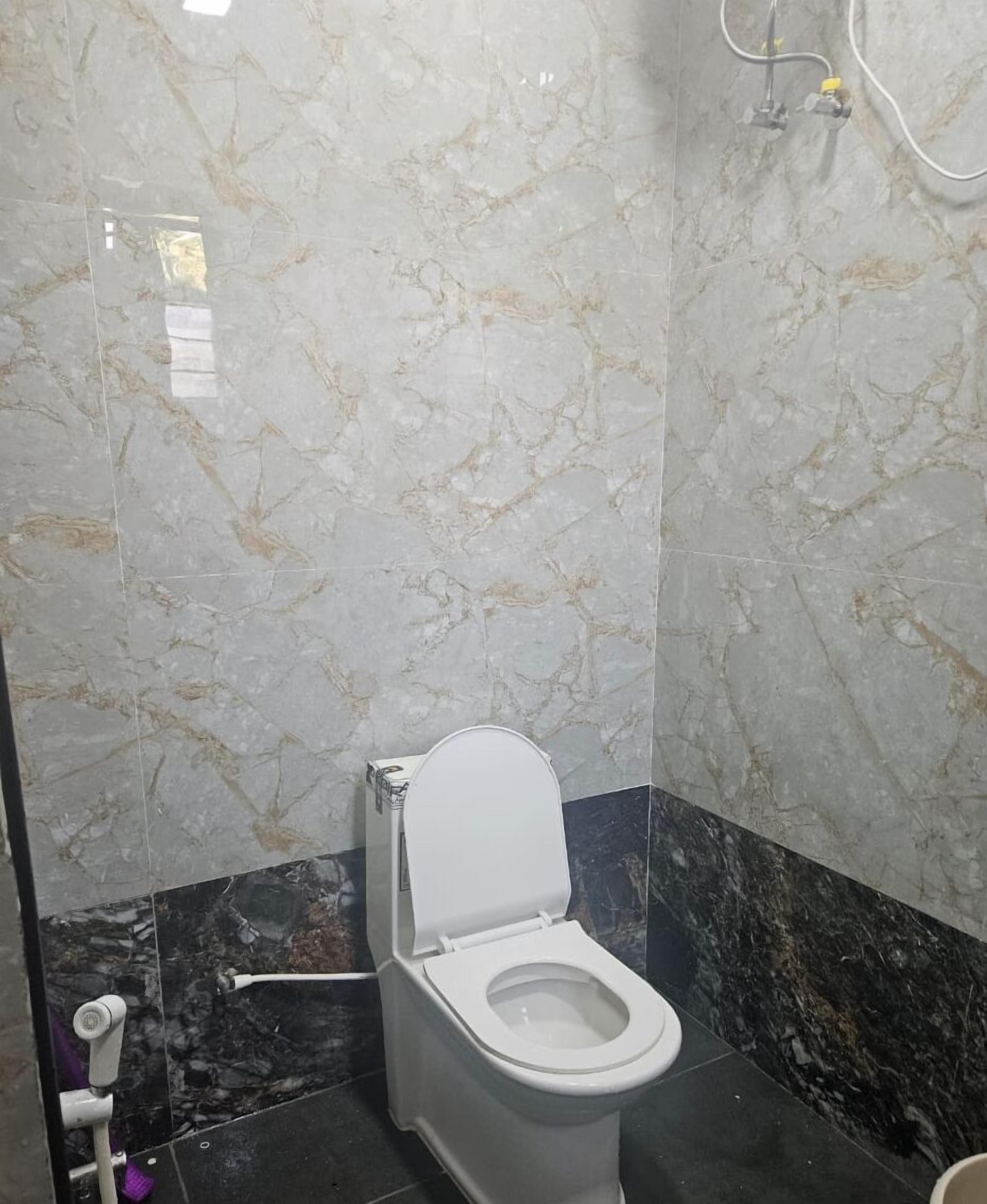 A bathroom with a toilet, marble walls, and a black marble floor.