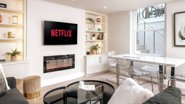 Un salon moderne doté d’une cheminée, d’un coin repas et d’un grand téléviseur affichant le logo « NETFLIX ».