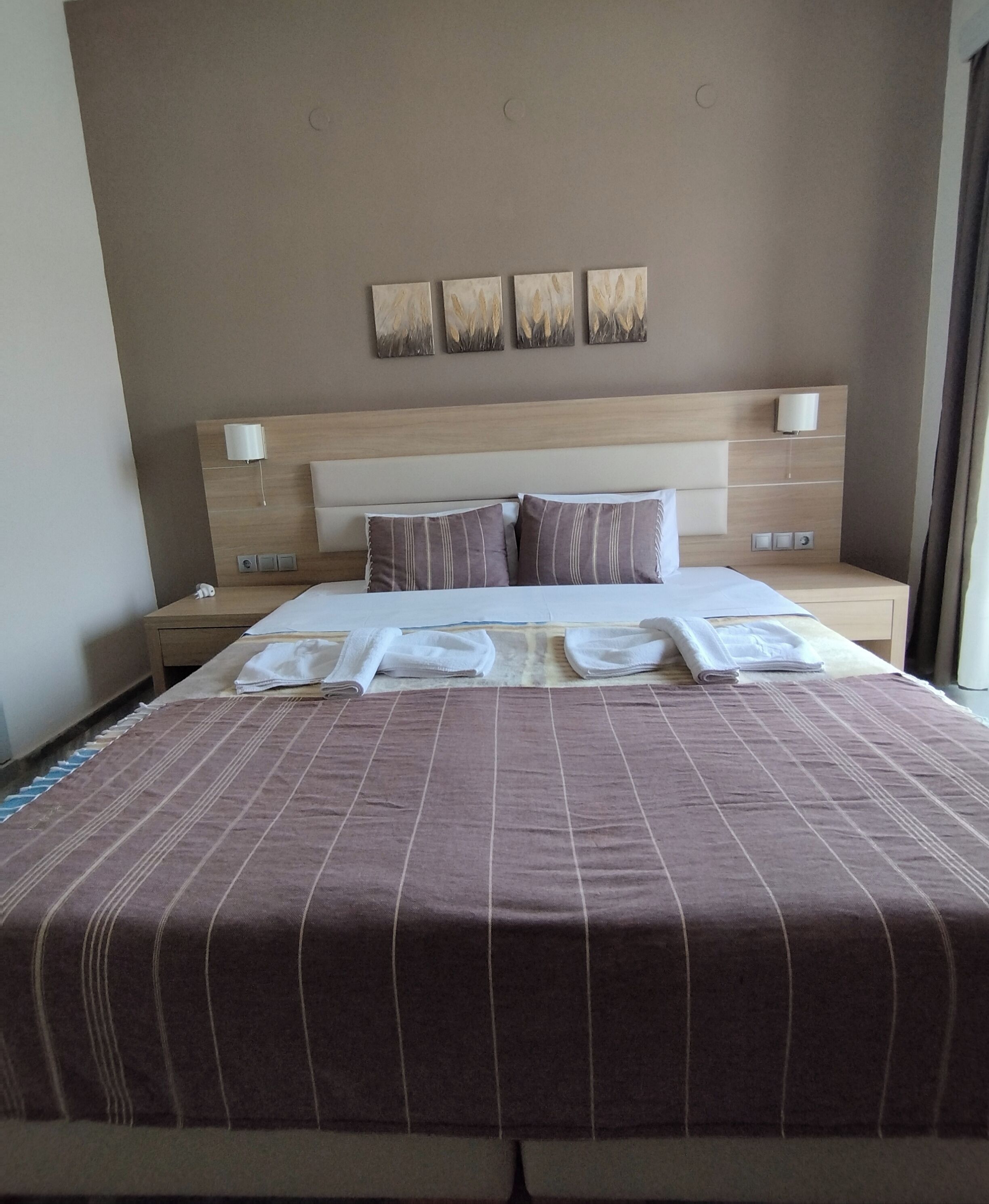 Habitación de hotel con una cama grande, ropa de cama a rayas, dos mesitas de noche con lámparas y una pared con cuatro cuadros enmarcados.