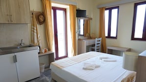 A hotel room with a bed, a desk, a chair, a TV, a sink, and a window. - Vida Balance Garden (Mithimna)