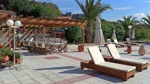 An outdoor patio with wooden lounge chairs, tables, and a pergola with hanging lights. - Vida Balance Garden (Mithimna)