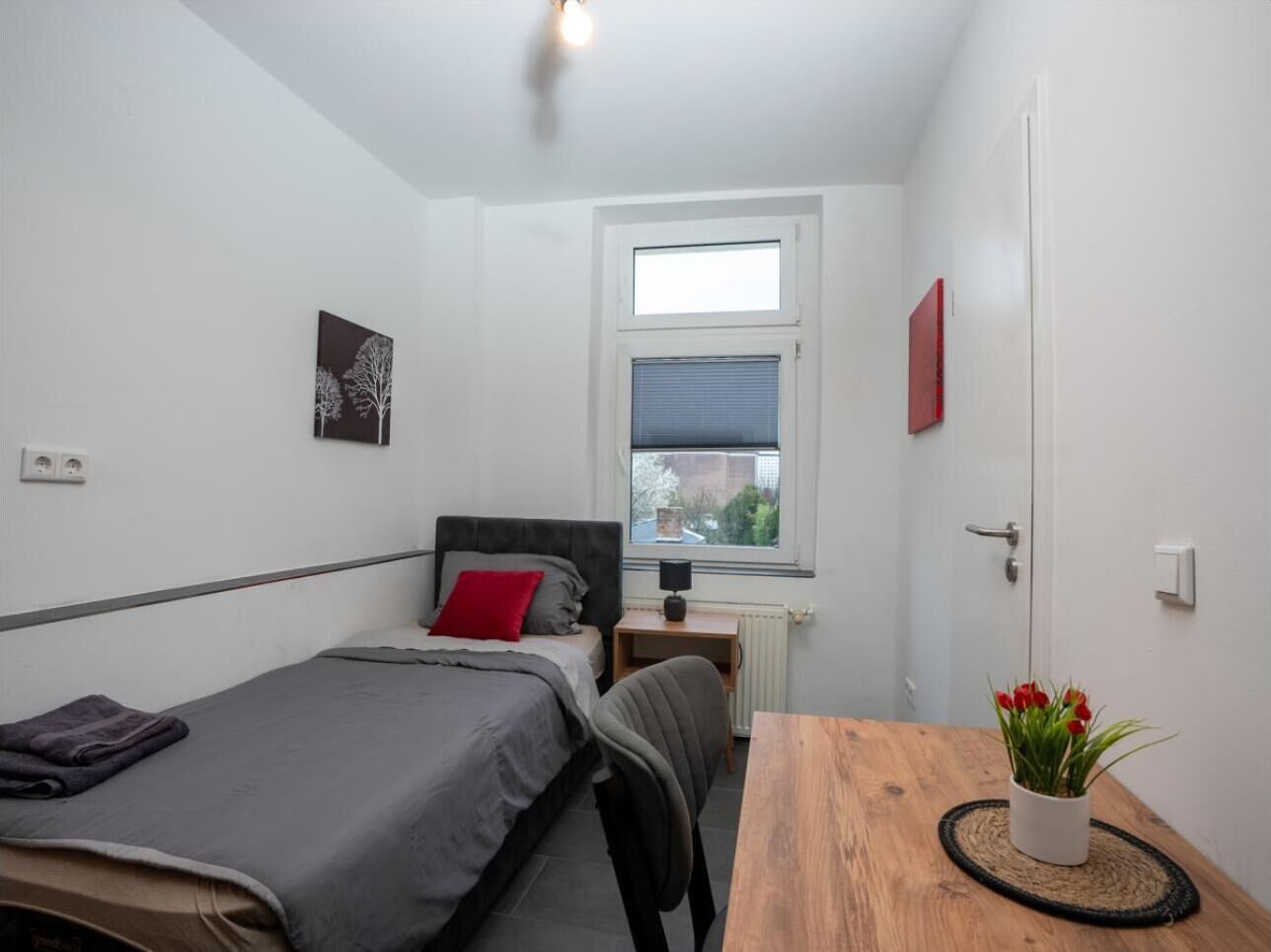 A small, clean room with a bed, bedside table, and a window.