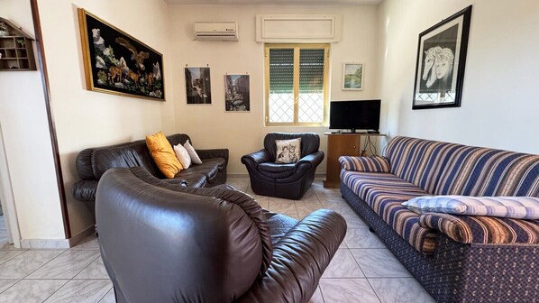 Una sala de estar con un sofá de cuero marrón, un sofá a rayas, un sillón de cuero negro y una mesita de madera.