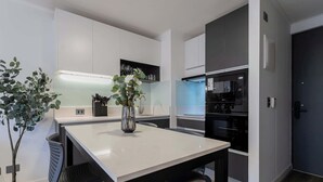 A modern kitchen with white cabinets, a black countertop, and a dining table with two chairs.