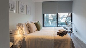 A modern bedroom with a large bed, a chair, and a view of the outside.