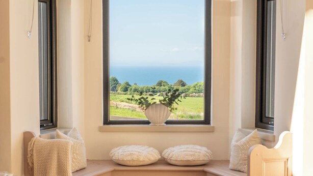 Un rincón con asientos y vistas al mar, una pequeña mesa con una vela y una concha decorativa.