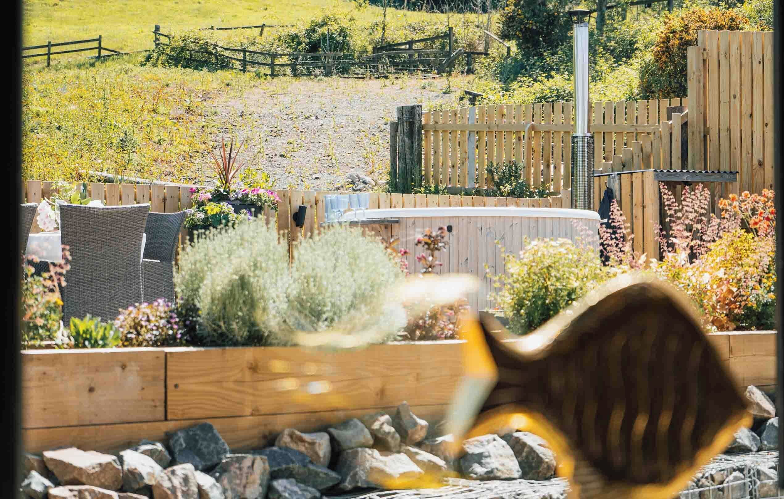 Un jardín con cerco de madera, jacuzzi y mobiliario exterior.