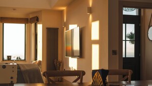 Una sala moderna con un sofá, una mesa de centro y un televisor montado en la pared. Hay una ventana con cortinas y una puerta con un espejo redondo.