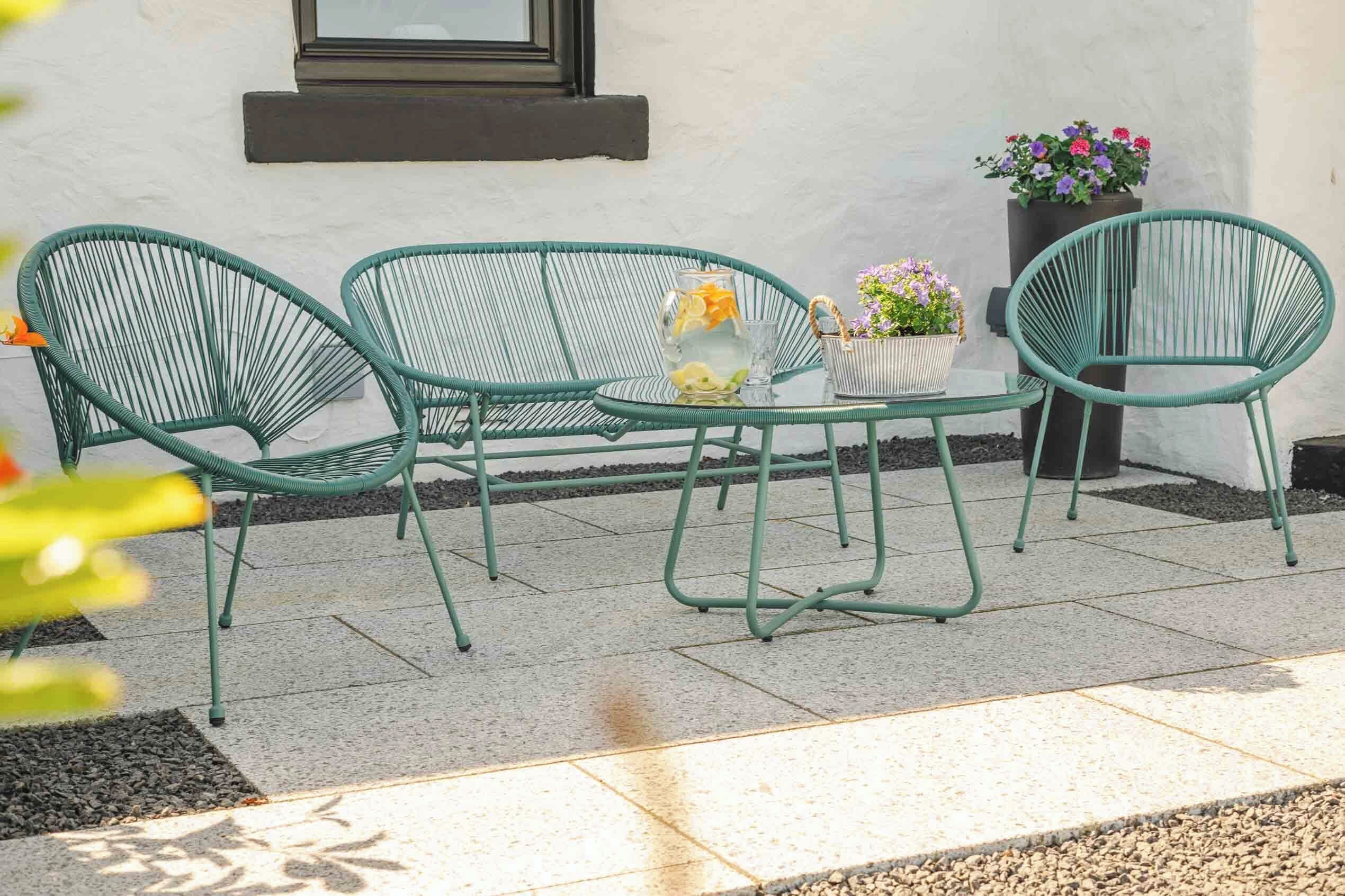 Et udendørs siddeområde i grønt metal med et bord, stole og plantekasser.