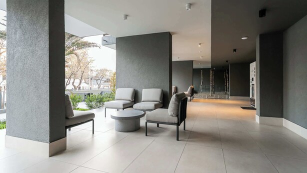 A modern indoor seating area with grey sofas and a round coffee table, large pillars, and a tiled floor.