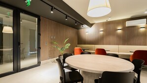A modern meeting room with a round table, black chairs, a potted plant, and a wooden panel wall.