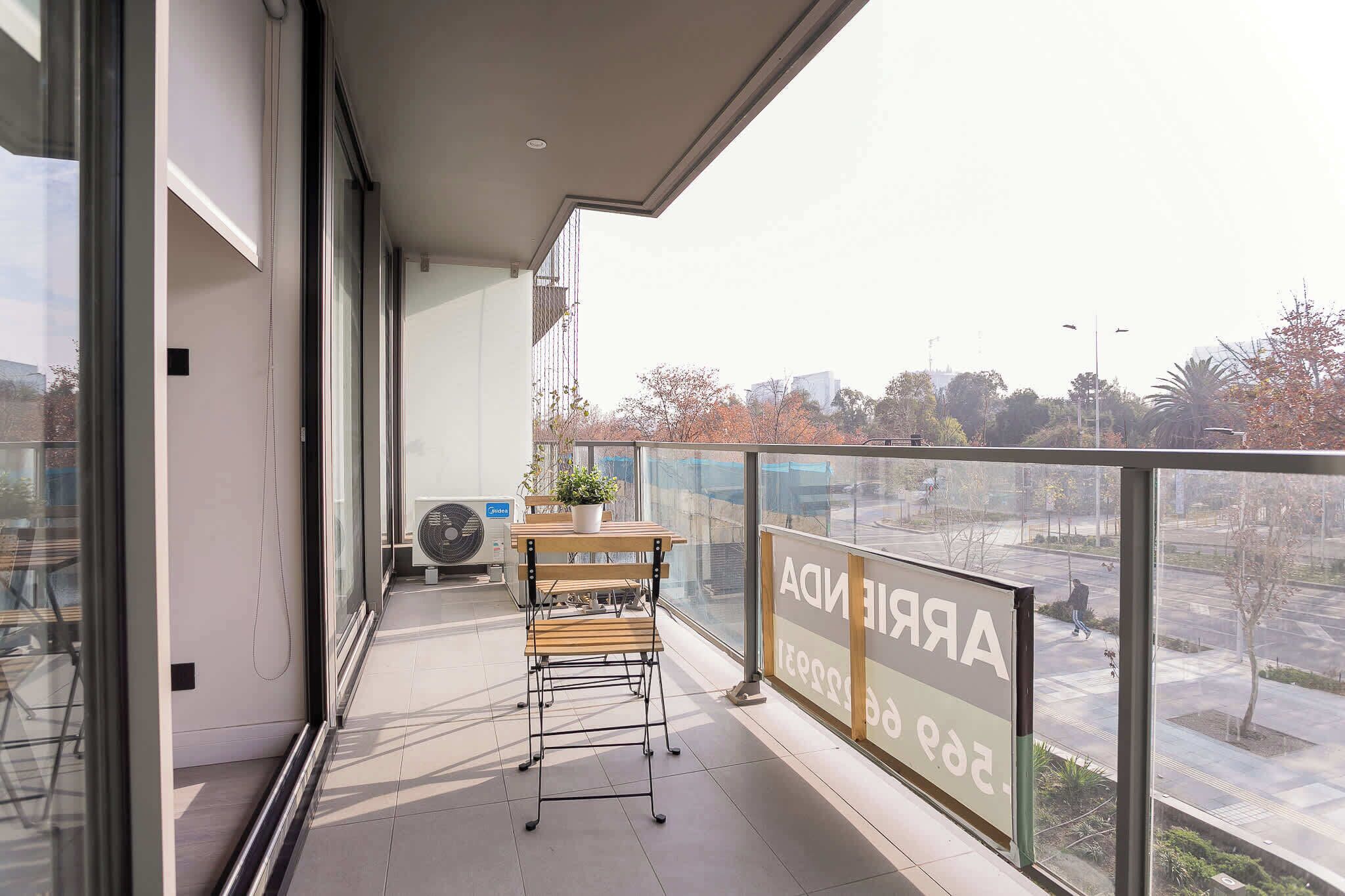A balcony with a table and chairs, a potted plant, and a view of a parking lot and trees.