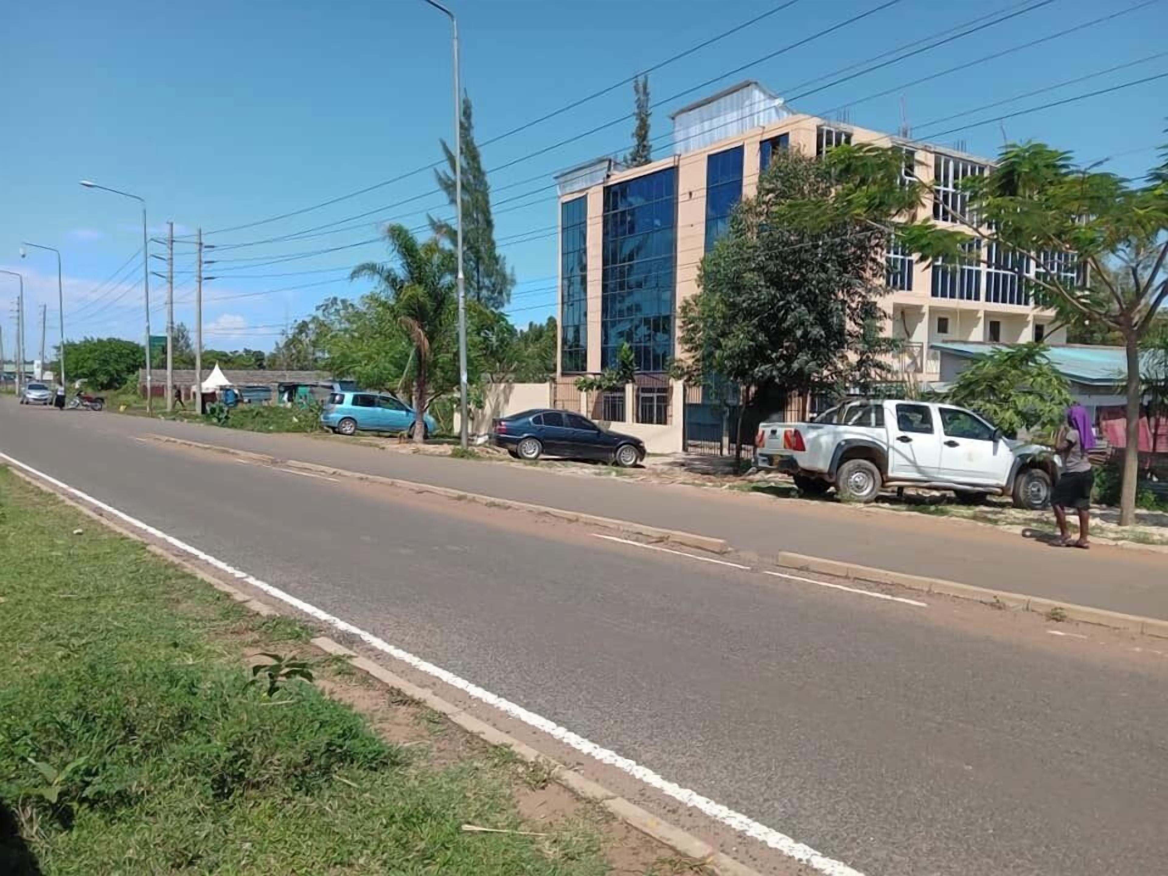 A street with a modern building, parked cars, and a clear sky.