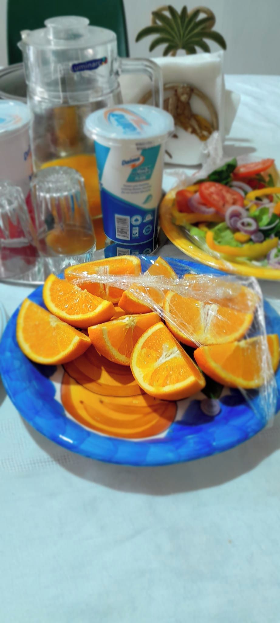 Een bord met sinaasappelschijfjes, een salade en een fles melk op een tafel.