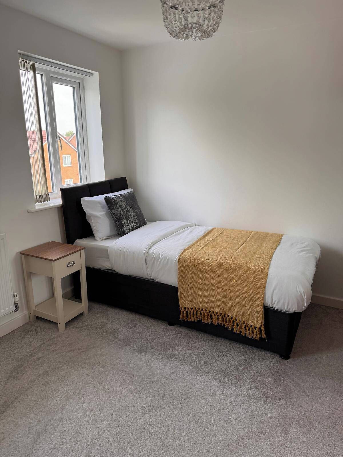 A bedroom with a bed, a bedside table, a window, and a chandelier.