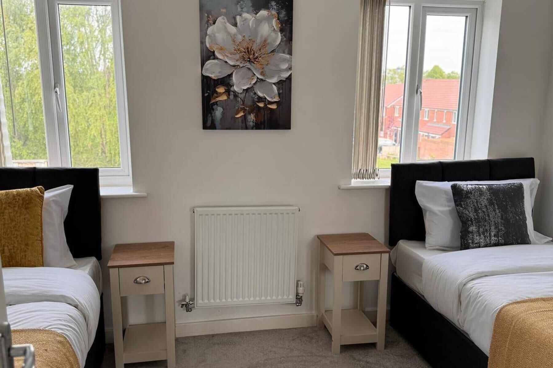 A bedroom with two beds, a radiator, and a painting of flowers on the wall.