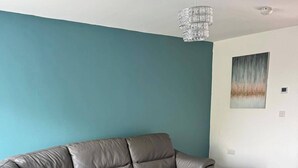 A modern living room with a sectional sofa, teal walls, and a minimalist decor. - House - Sleeps 6 - Parking (Coventry)