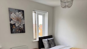 A bedroom with two beds, a radiator, a window with curtains, a painting, and a chandelier. - House - Sleeps 6 - Parking (Coventry)