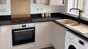 A modern kitchen with a built-in oven, a sink, and a washing machine. - House - Sleeps 6 - Parking (Coventry)