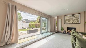 A spacious living room with a large sliding glass door leading to a patio, a green sofa, and a fireplace. - Spacious Family Home near Windsor - By Tempstay (Berkshire)