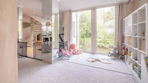 A spacious room with a large window, a staircase, and a bookshelf. - Spacious Family Home near Windsor - By Tempstay (Berkshire)