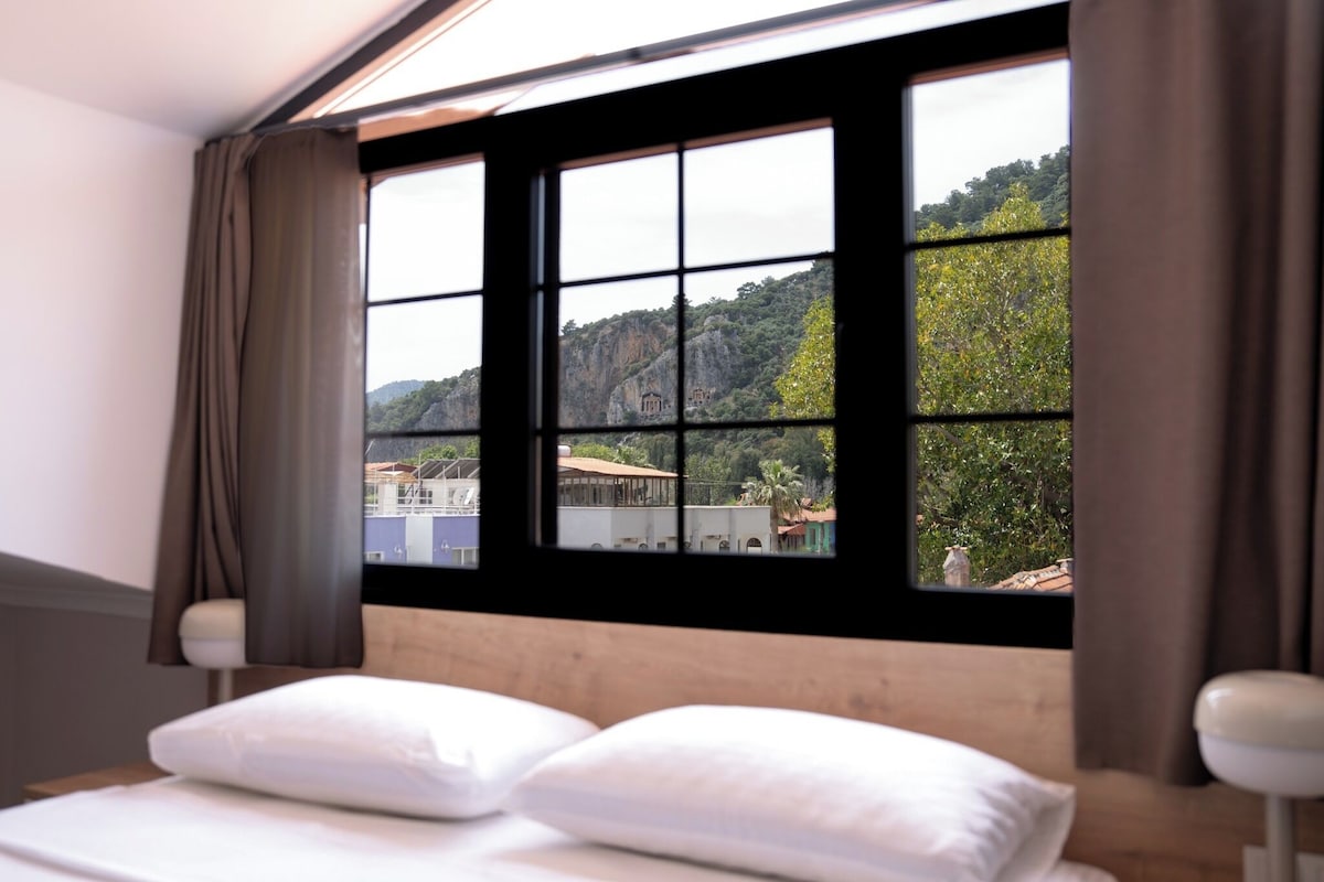 A bedroom with a large window, a bed with white bedding, and curtains.